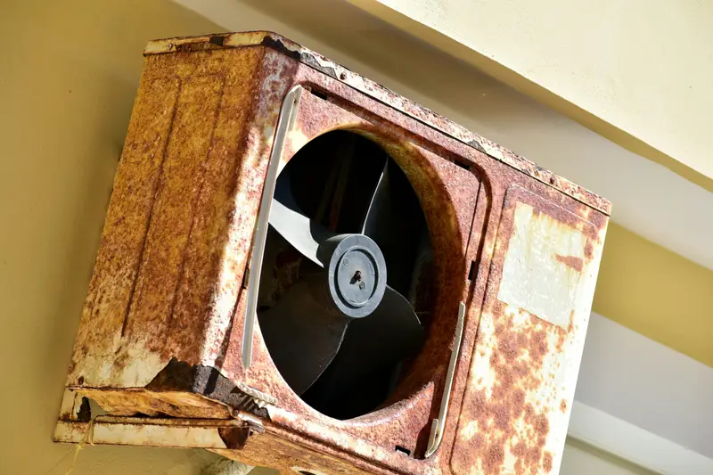 a rusted metal fan mounted to the side of a building